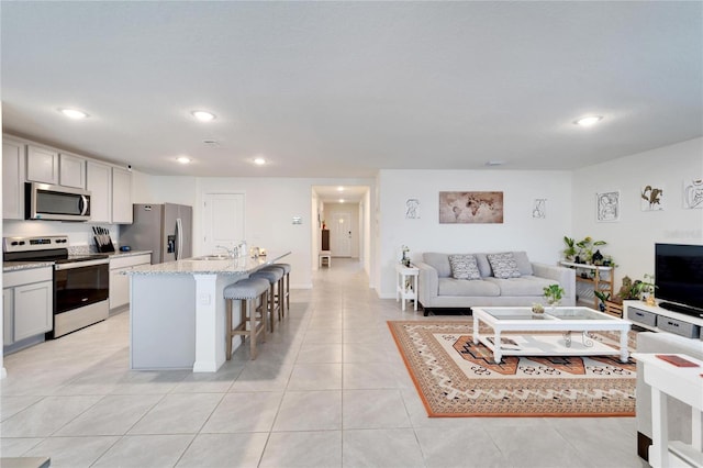 kitchen featuring a breakfast bar area, light tile patterned floors, a kitchen island with sink, appliances with stainless steel finishes, and sink