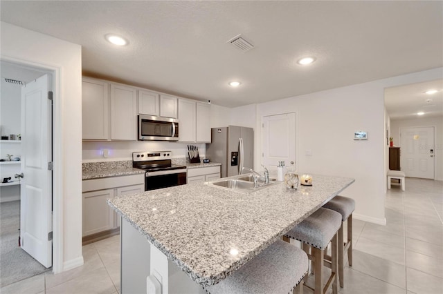 kitchen with sink, appliances with stainless steel finishes, a center island with sink, and light tile patterned floors