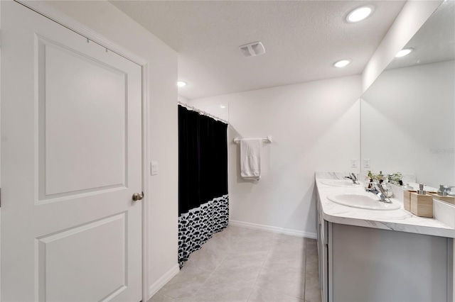 bathroom with a textured ceiling, tile patterned flooring, and dual bowl vanity