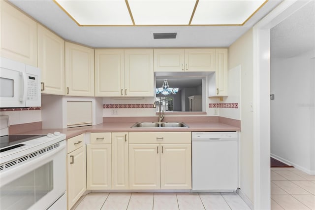 kitchen with white appliances, sink, light tile patterned floors, an inviting chandelier, and cream cabinetry