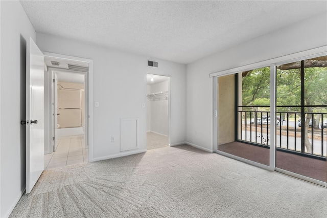 unfurnished bedroom with a spacious closet, a textured ceiling, access to outside, light carpet, and a closet