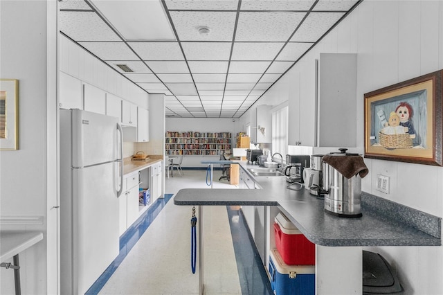 kitchen featuring white cabinets, a drop ceiling, white refrigerator, and sink