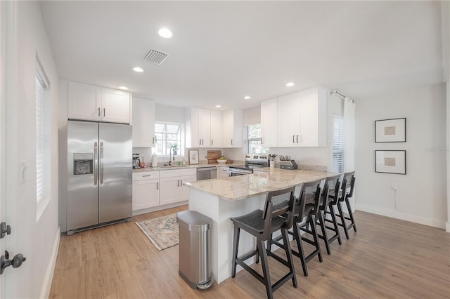 kitchen with light wood-type flooring, stainless steel appliances, white cabinetry, kitchen peninsula, and a breakfast bar area