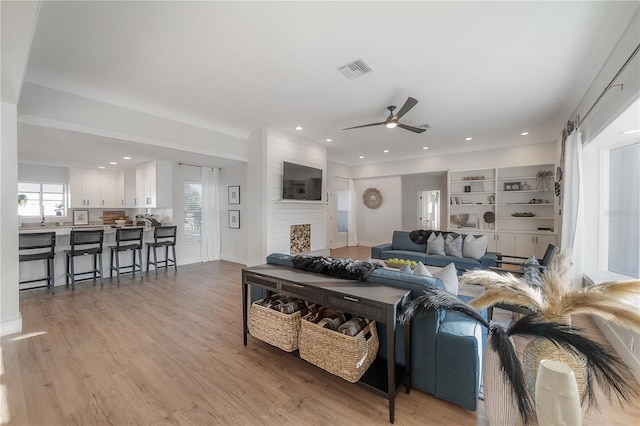 living room with light wood-type flooring, ceiling fan, and a fireplace