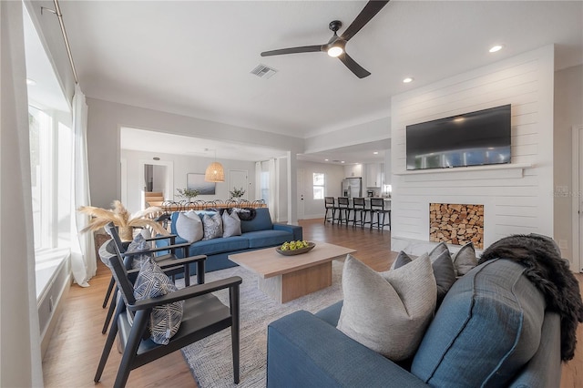 living room featuring light wood-type flooring, ceiling fan, and a large fireplace