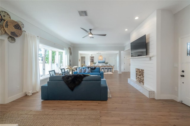 living room featuring wood-type flooring, ceiling fan, and a large fireplace