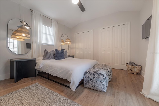 bedroom with lofted ceiling, ceiling fan, two closets, and hardwood / wood-style flooring