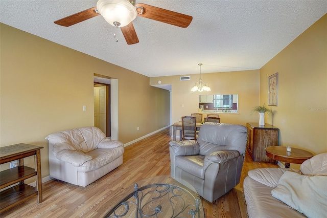 living room with ceiling fan with notable chandelier, a textured ceiling, and light hardwood / wood-style flooring