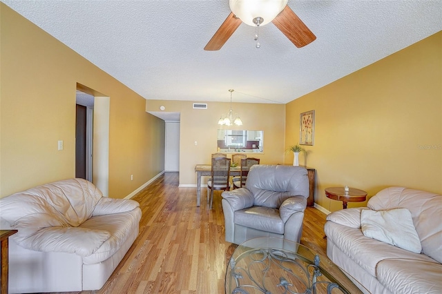 living room featuring ceiling fan with notable chandelier, light hardwood / wood-style floors, and a textured ceiling