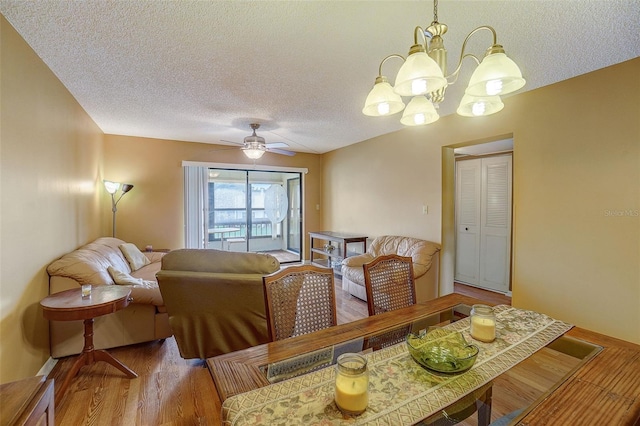 dining area with hardwood / wood-style floors, ceiling fan with notable chandelier, and a textured ceiling