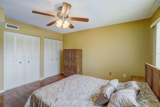 bedroom with two closets, ceiling fan, dark hardwood / wood-style flooring, and a textured ceiling