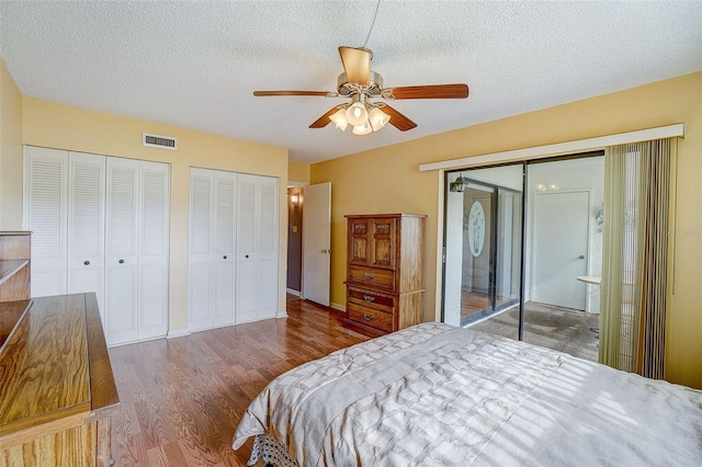 bedroom with a textured ceiling, ceiling fan, two closets, and hardwood / wood-style flooring