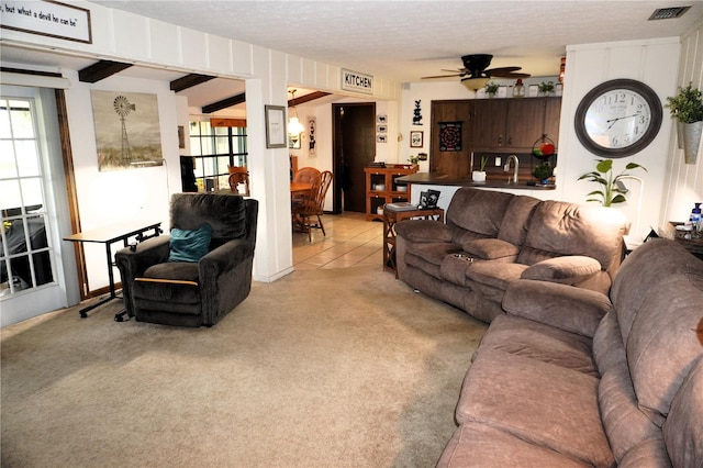 tiled living room featuring beamed ceiling, ceiling fan, a textured ceiling, and sink