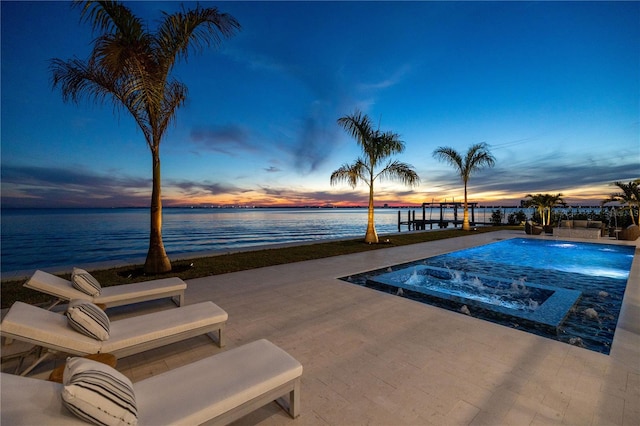 pool at dusk with a water view and a patio area