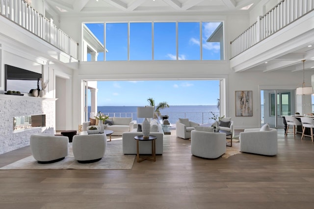 living room featuring a high ceiling, a water view, wood-type flooring, and beam ceiling