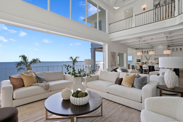 living room with light hardwood / wood-style floors, a water view, and a high ceiling