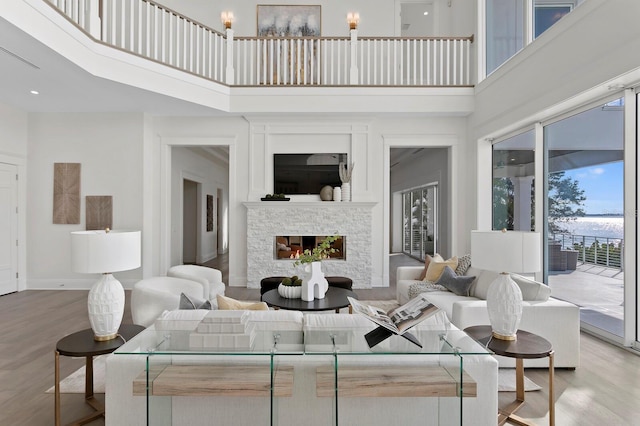 living room with a stone fireplace, a towering ceiling, and wood-type flooring