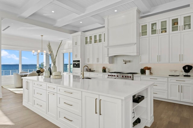 kitchen featuring white cabinets, a water view, sink, and an island with sink