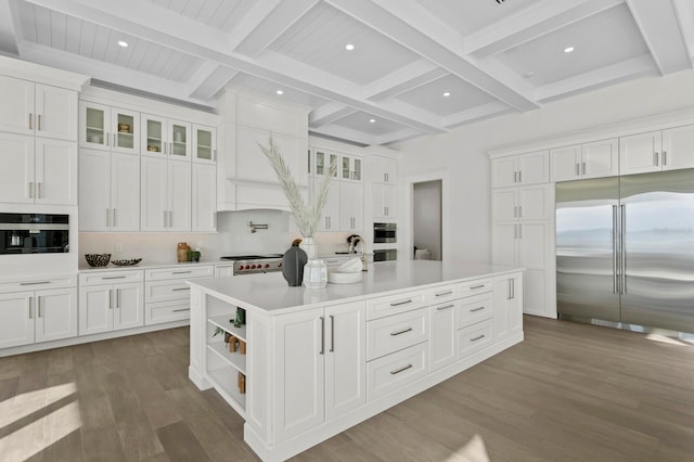 kitchen with wood-type flooring, a kitchen island with sink, beam ceiling, white cabinetry, and appliances with stainless steel finishes