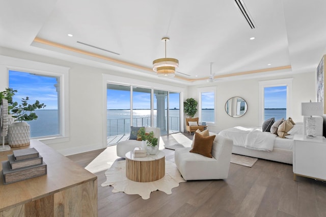 bedroom with dark wood-type flooring, access to outside, a water view, and a raised ceiling