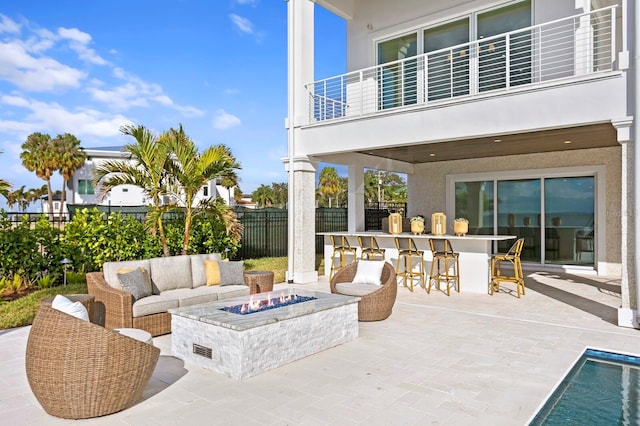 view of patio featuring a balcony, exterior bar, and an outdoor living space with a fire pit