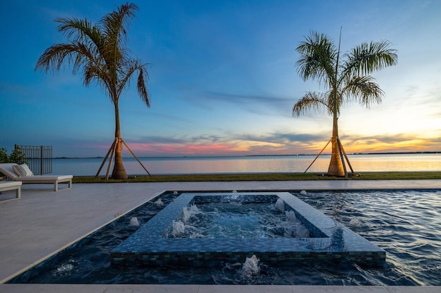 pool at dusk with a water view and an in ground hot tub