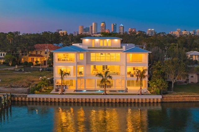 back house at dusk featuring a water view, a balcony, and a patio area