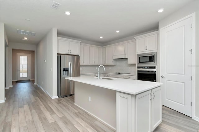 kitchen with a center island with sink, black appliances, custom range hood, and light wood-type flooring