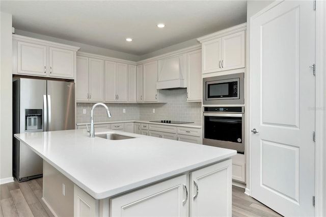 kitchen with custom range hood, an island with sink, appliances with stainless steel finishes, decorative backsplash, and sink