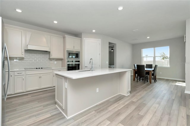 kitchen featuring light wood-type flooring, backsplash, custom exhaust hood, appliances with stainless steel finishes, and sink