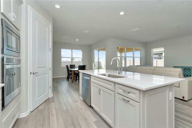 kitchen with appliances with stainless steel finishes, sink, light hardwood / wood-style floors, and an island with sink