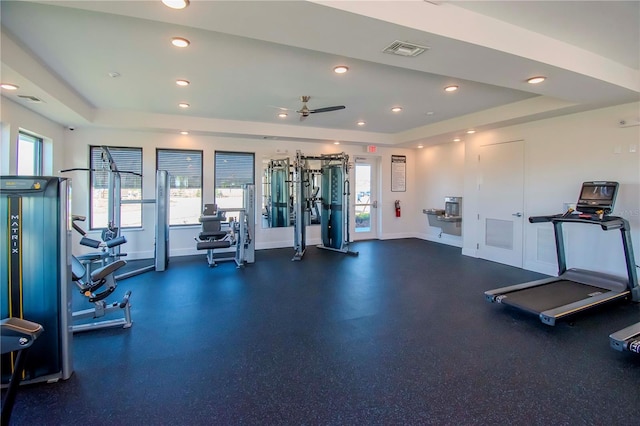 gym with ceiling fan and a tray ceiling