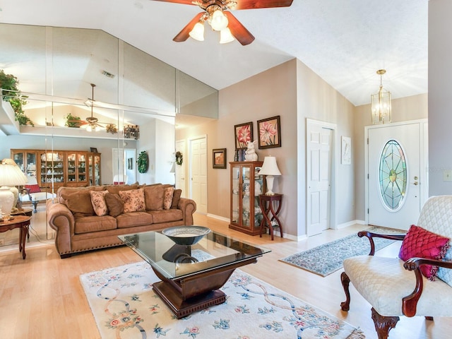 living room featuring high vaulted ceiling, ceiling fan with notable chandelier, and light wood-type flooring