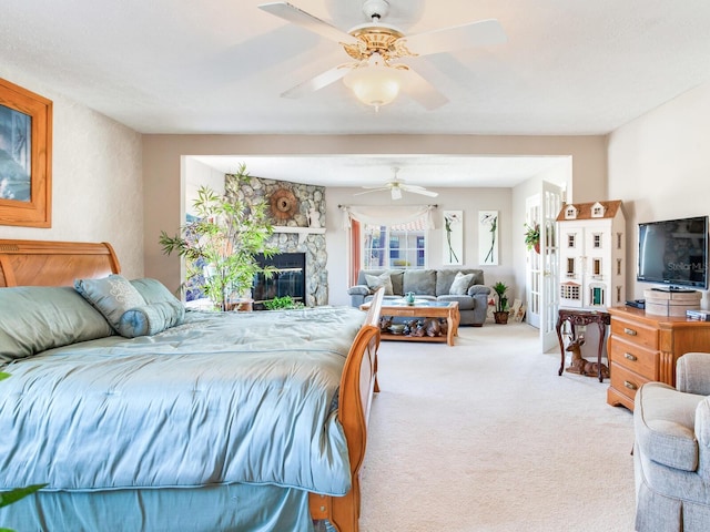 bedroom with a stone fireplace, ceiling fan, and light colored carpet