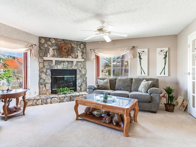 living room with light carpet, a textured ceiling, ceiling fan, and a stone fireplace