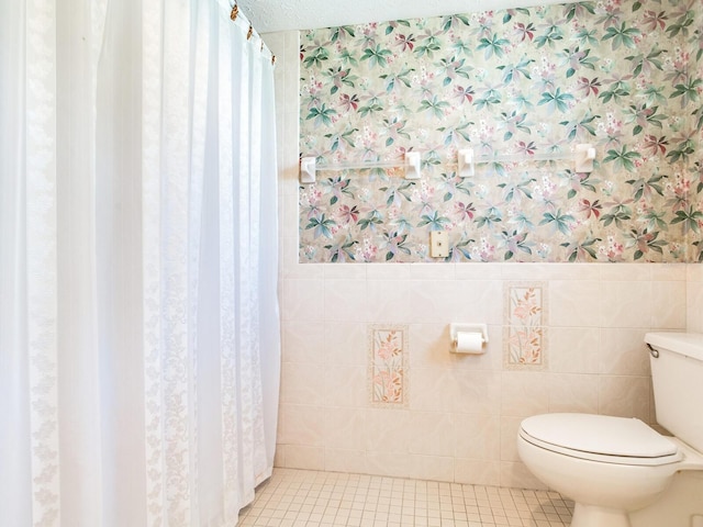 bathroom with toilet, tile flooring, a textured ceiling, and tile walls