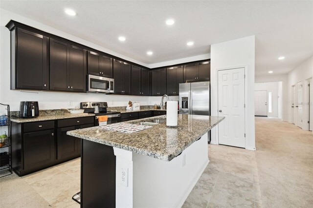 kitchen featuring a breakfast bar area, a kitchen island with sink, stainless steel appliances, stone counters, and sink