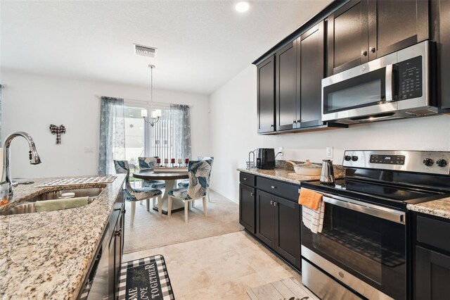 kitchen with light tile patterned flooring, an inviting chandelier, light stone countertops, appliances with stainless steel finishes, and sink