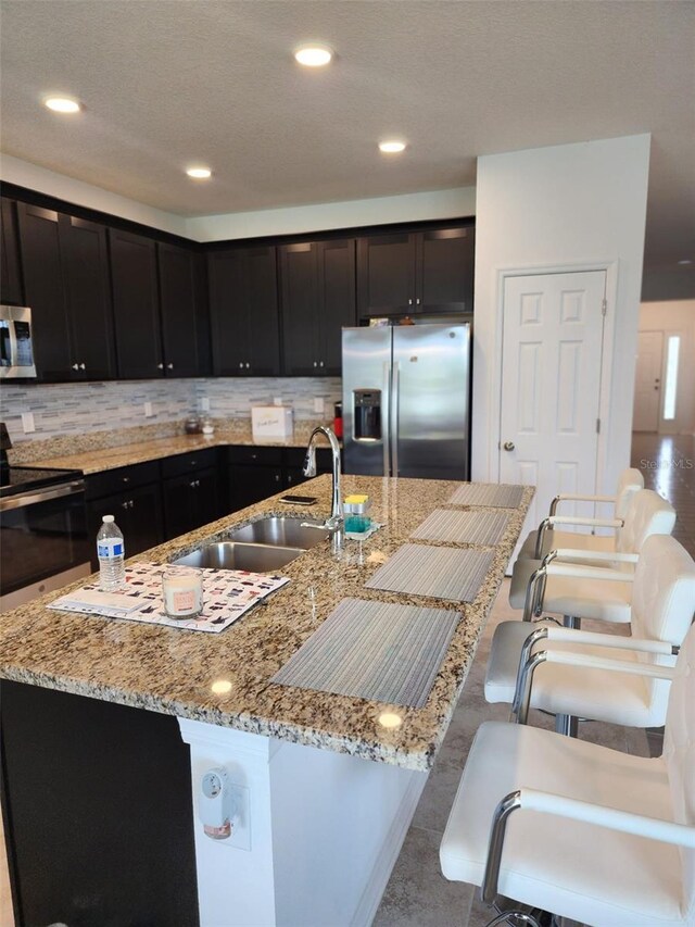 kitchen with backsplash, light stone counters, appliances with stainless steel finishes, and sink