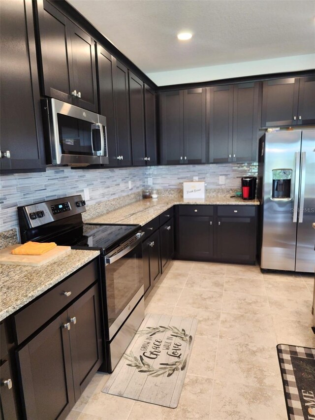 kitchen with light tile patterned floors, tasteful backsplash, light stone counters, and stainless steel appliances