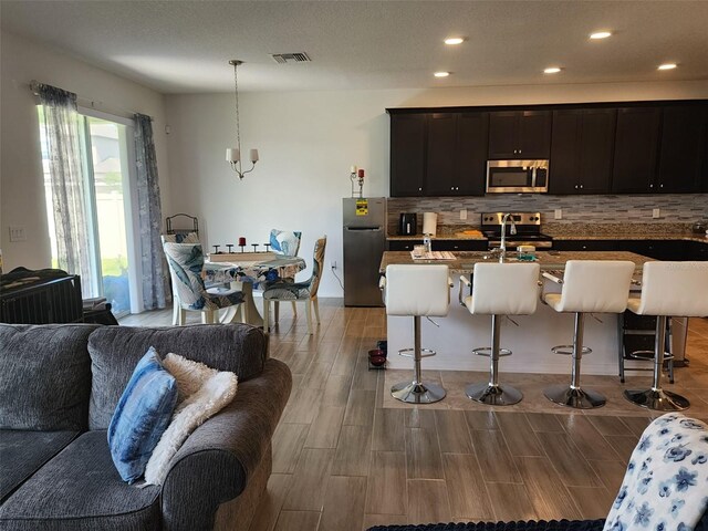 kitchen with appliances with stainless steel finishes, light hardwood / wood-style flooring, an inviting chandelier, and a breakfast bar area