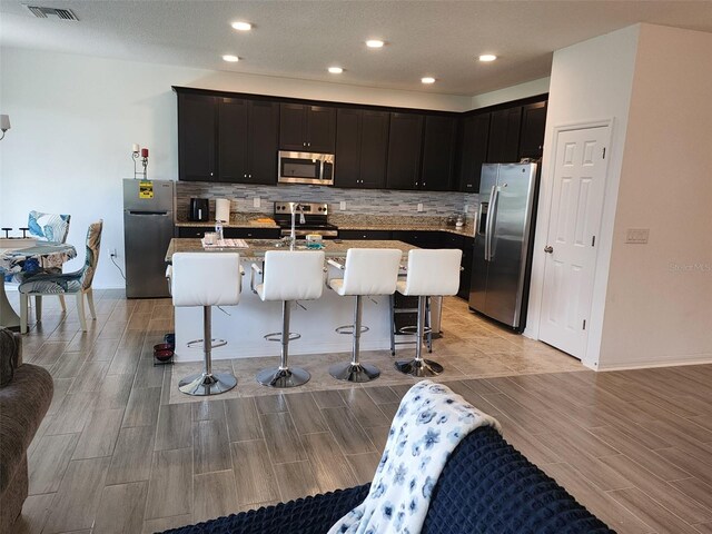 kitchen featuring decorative backsplash, appliances with stainless steel finishes, a center island with sink, and a breakfast bar