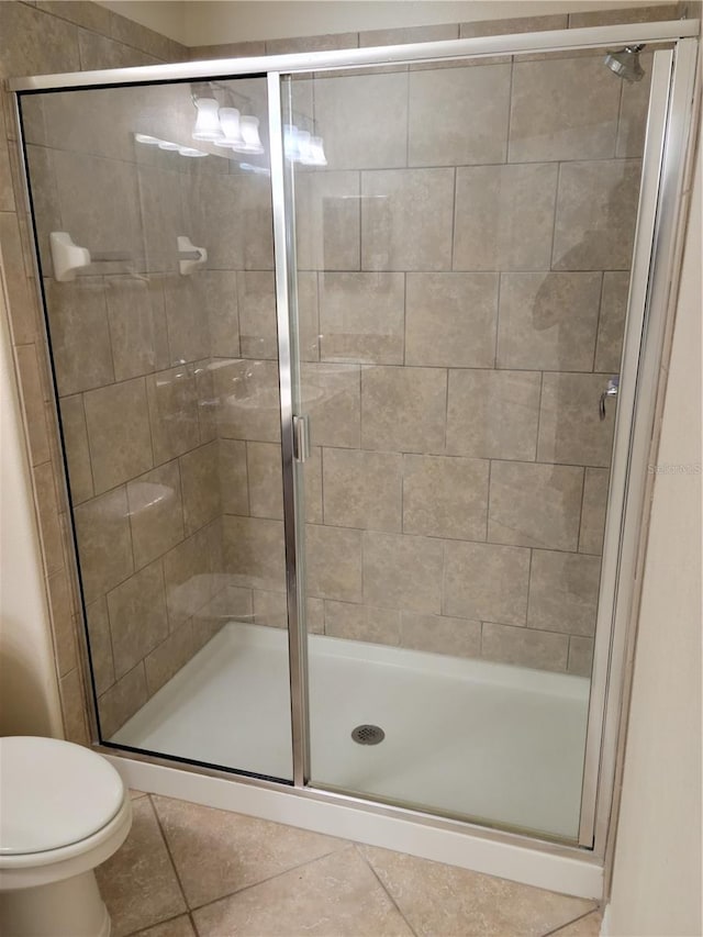 bathroom with toilet, a shower with shower door, and tile flooring