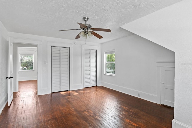 unfurnished bedroom featuring two closets, ceiling fan, dark wood-type flooring, and a textured ceiling