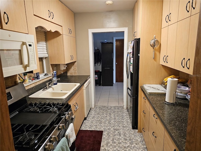 kitchen with white appliances, dark stone counters, light brown cabinetry, and sink