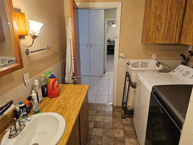 clothes washing area featuring sink, washing machine and dryer, and tile walls