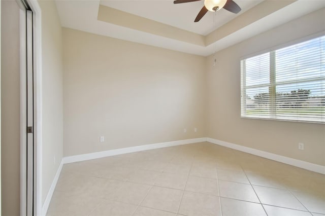 empty room with a raised ceiling, light tile patterned flooring, and ceiling fan