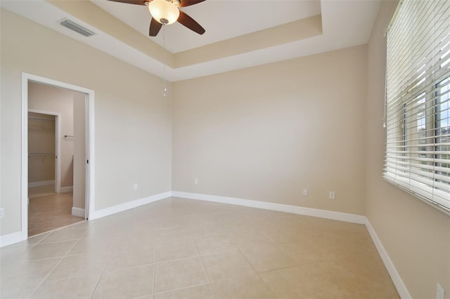 tiled empty room with a raised ceiling and ceiling fan