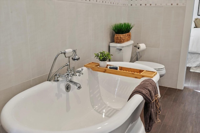 bathroom featuring tile walls, a tub, hardwood / wood-style floors, and toilet