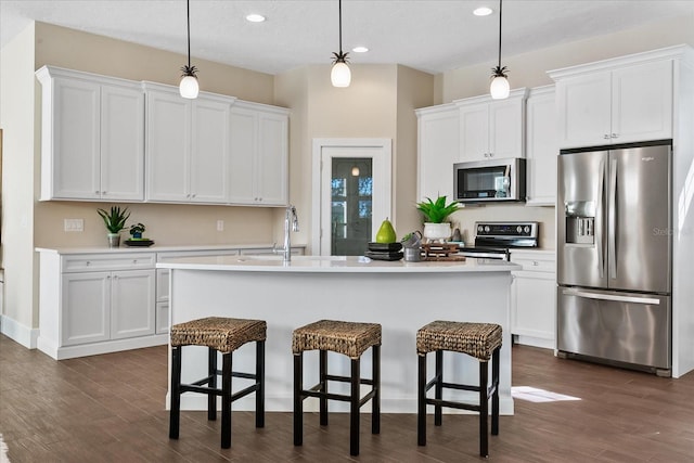 kitchen with appliances with stainless steel finishes, white cabinets, dark wood-type flooring, hanging light fixtures, and a center island with sink